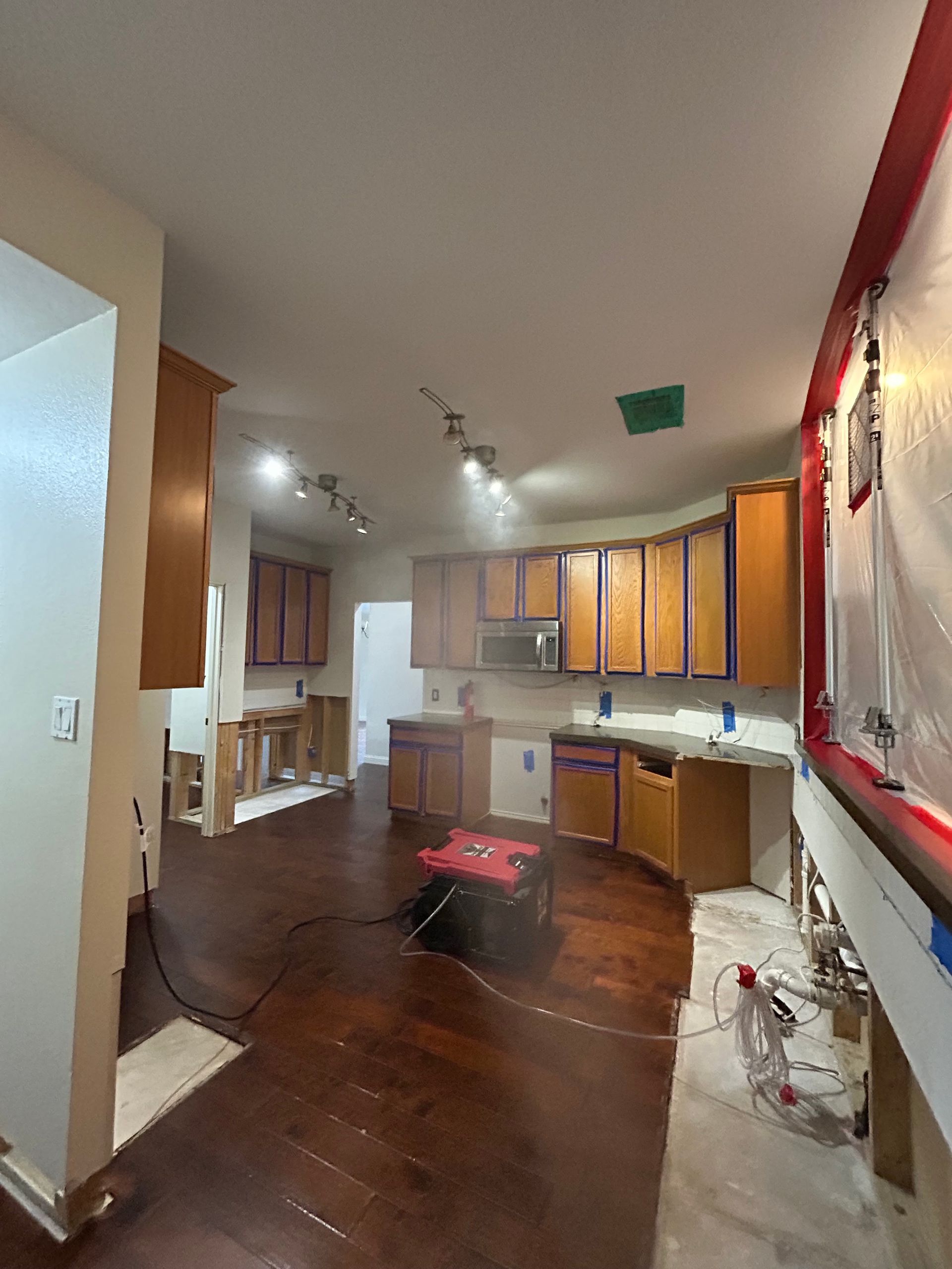 Empty kitchen with wood cabinets, dark hardwood floors, and a red-framed wall mirror.