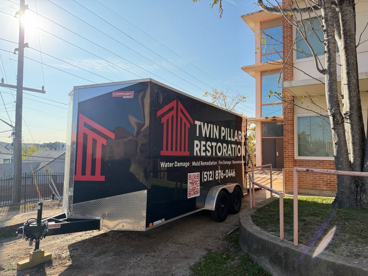 Branded black trailer for Twin Pines Restoration parked beside an apartment building in bright sunlight