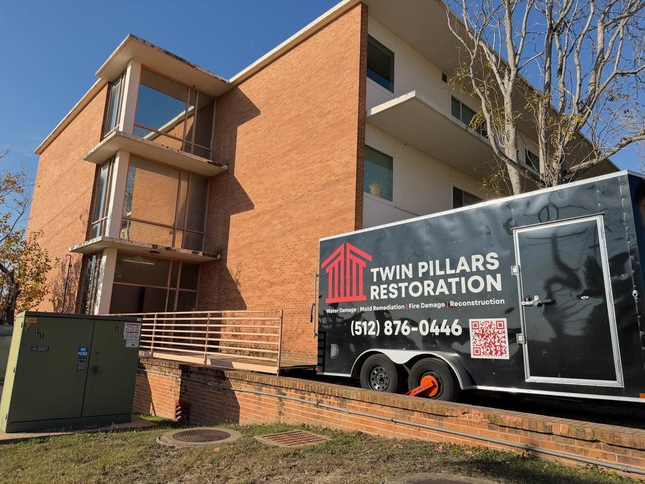 Brick apartment building beside a Twin Pillars Restoration truck and equipment trailer.