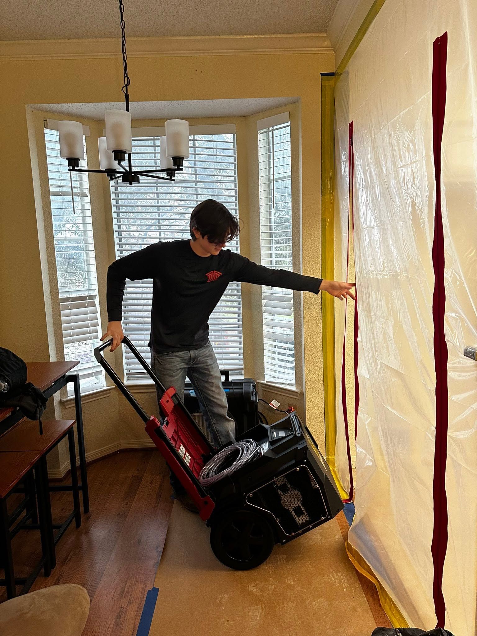 Person beside a tipped-over black stroller in a bright room with wood floors and shuttered windows