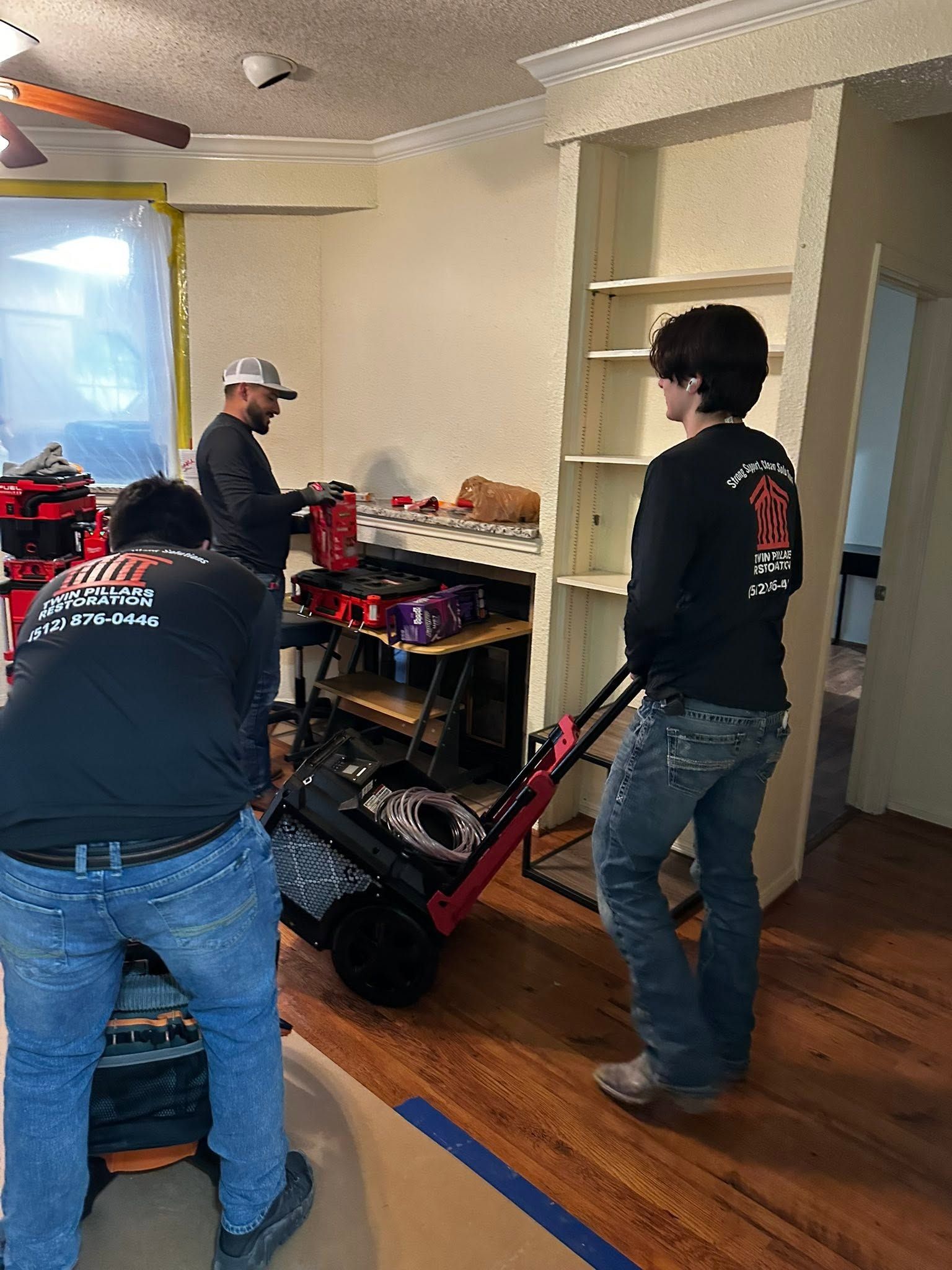 Three people moving furniture in a living room with hardwood floors and scattered items