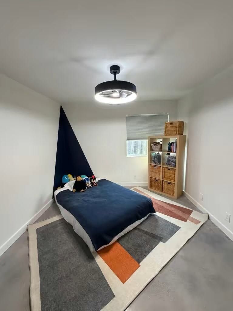 Small bedroom with a low bed, geometric rug, shelving, and a black ceiling light.