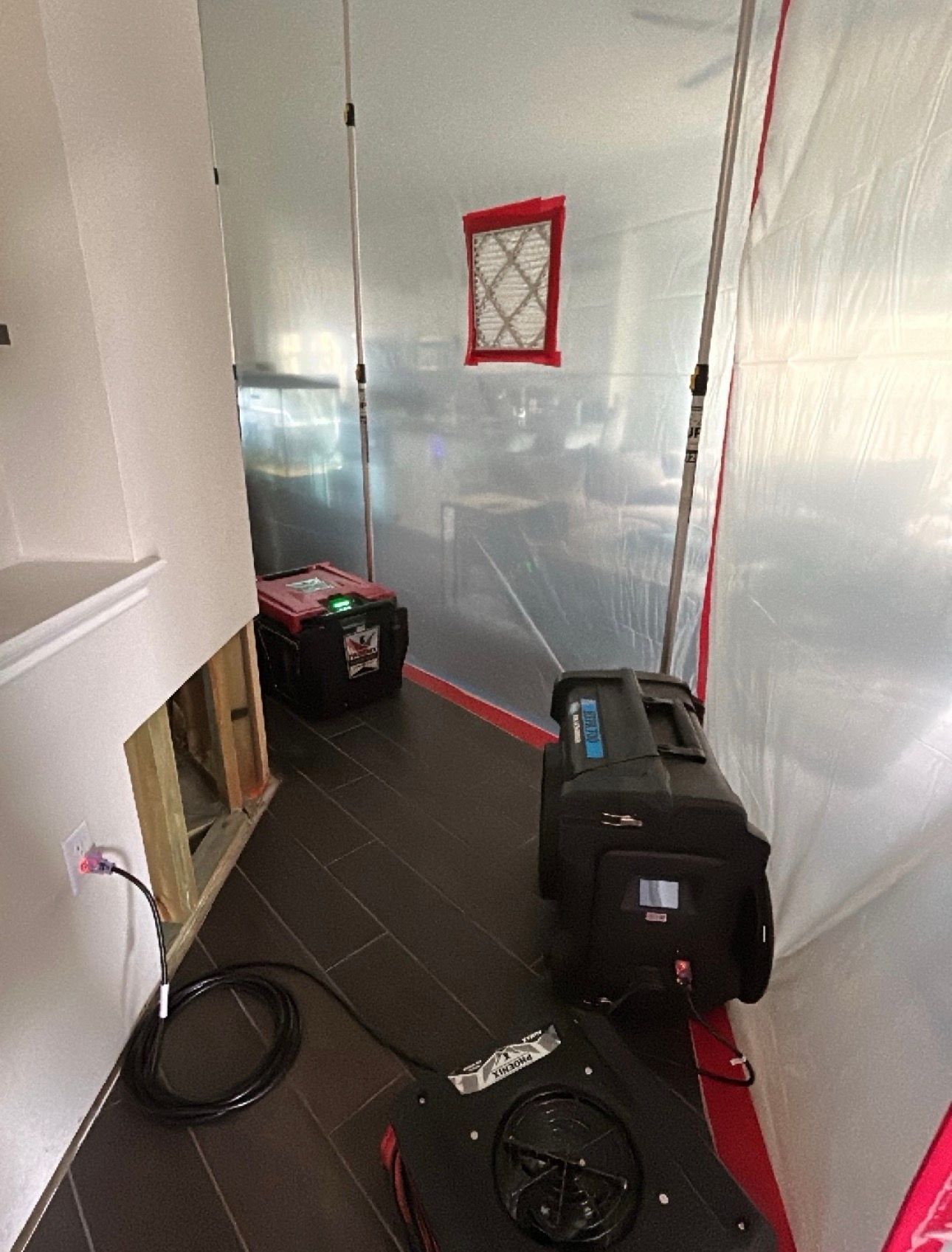 Narrow hallway with plastic-covered walls, a red-framed window, and two black equipment cases on the floor.