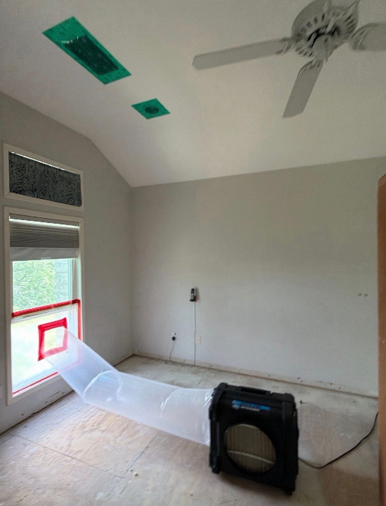 Empty room with fan, window ventilation setup, and a portable air blower on the floor.