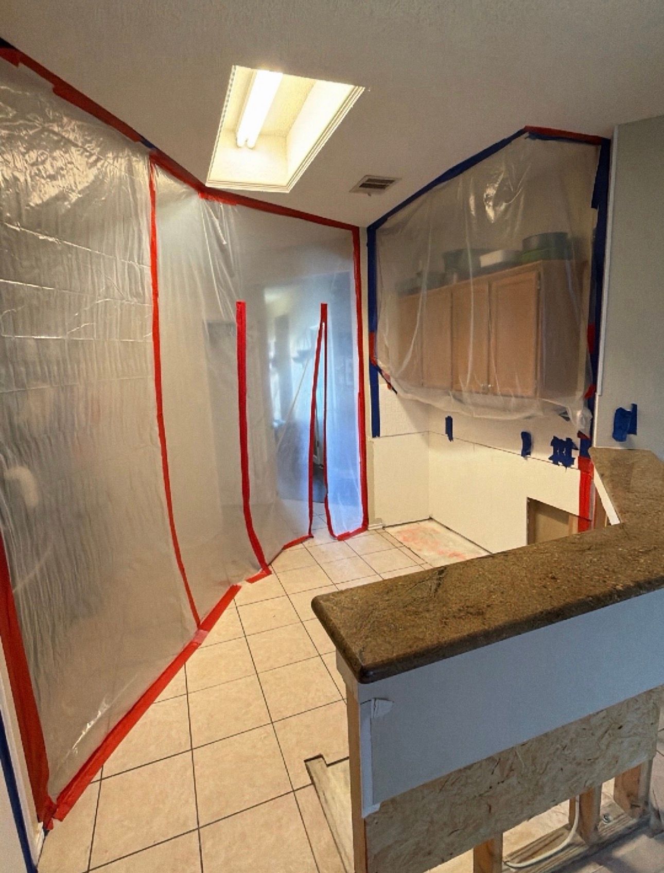 Kitchen under renovation, with plastic-covered walls, red tape, and a tiled floor.