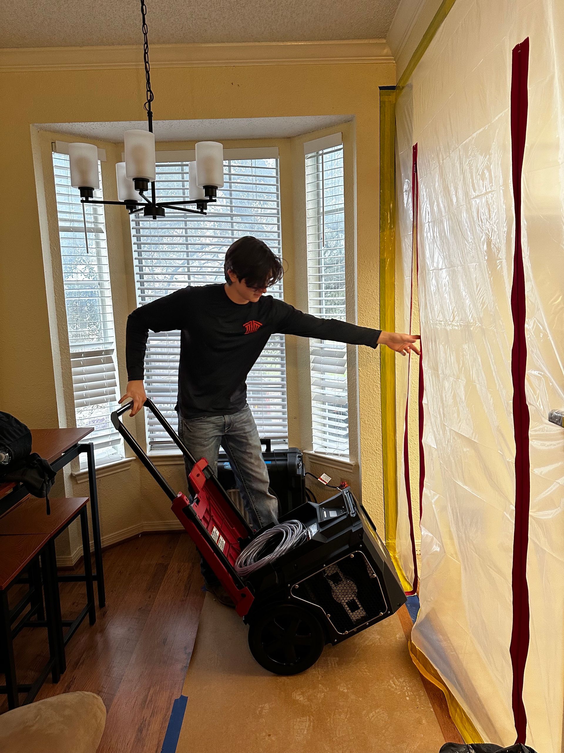 Person leaning from a chair to move a large black appliance in a narrow hallway with yellow walls.