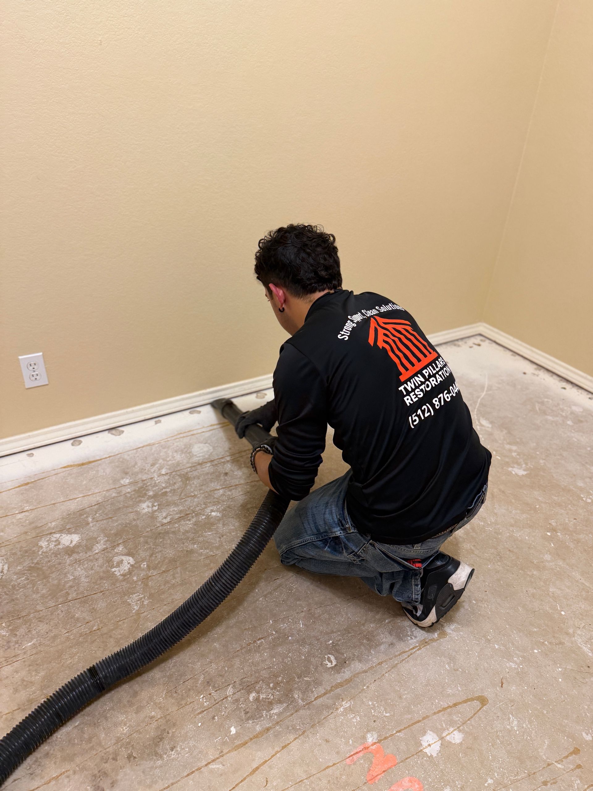 Worker kneeling to vacuum dust from a beige carpet along a wall during renovation
