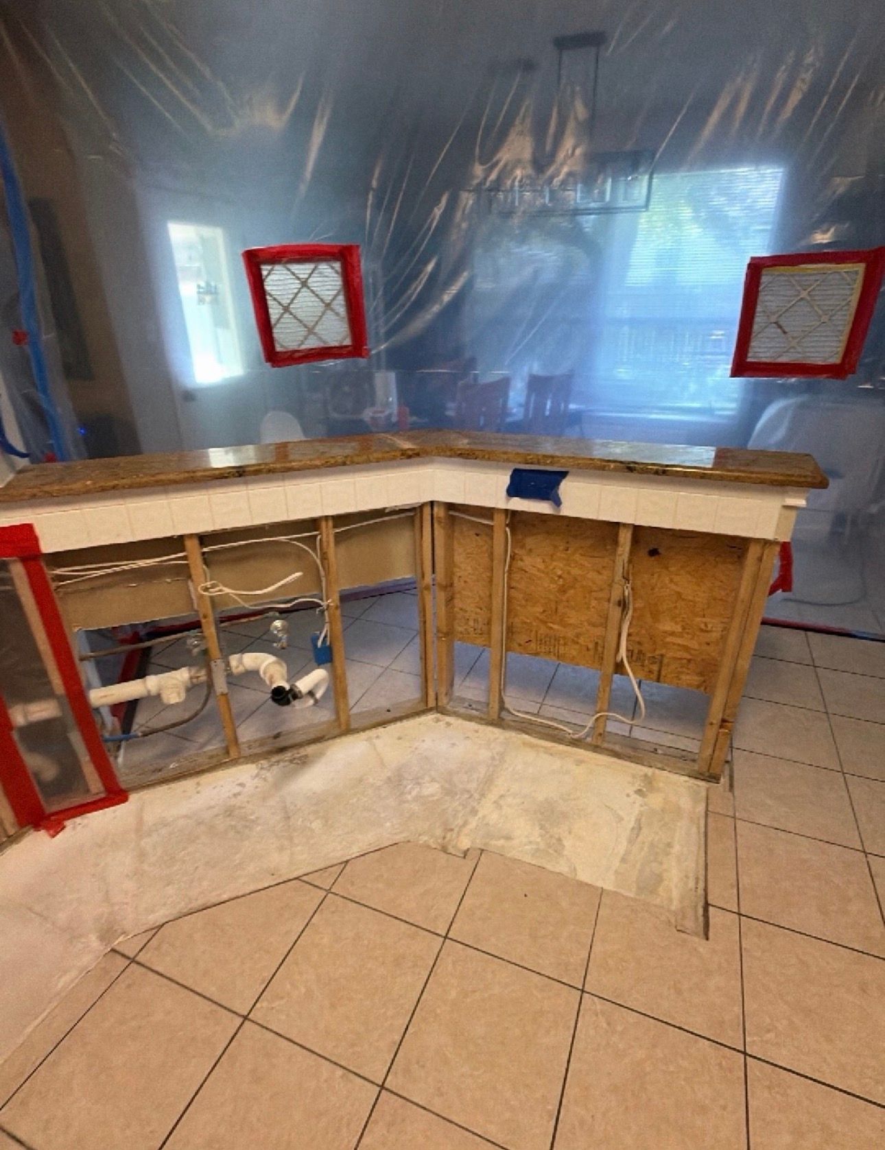 Kitchen under renovation with plastic-covered walls, exposed cabinets, and tiled floor.
