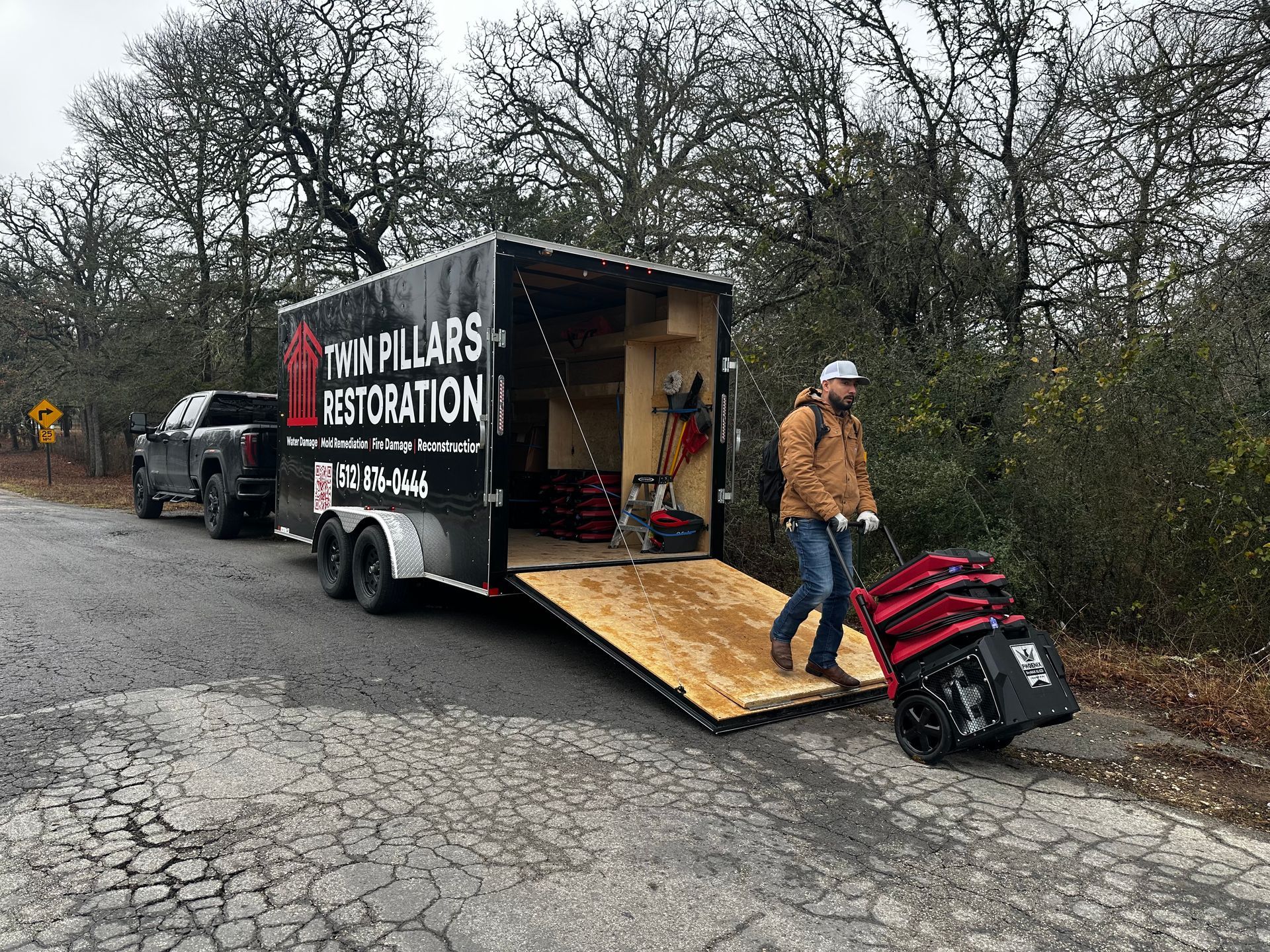 Worker unloading supplies from a trailer on a rural roadside near parked truck