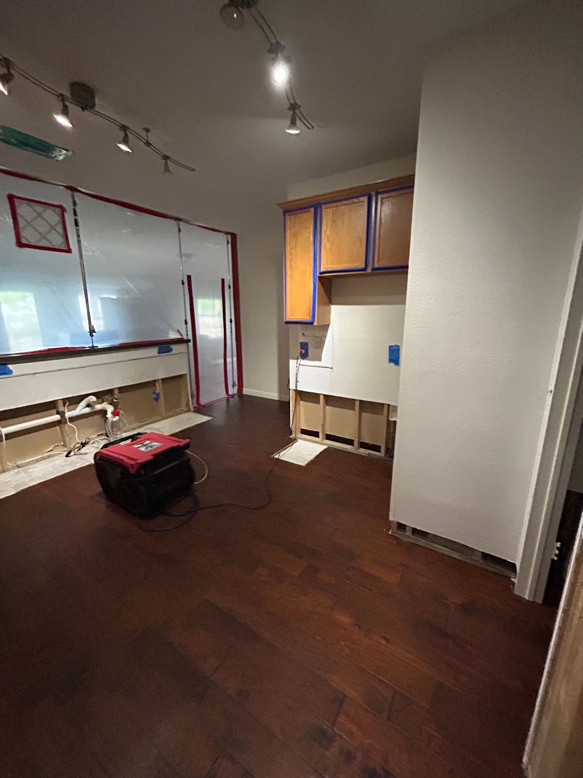 Empty room with dark wood floor, whiteboard, open cabinet, and a red toolbox under ceiling track lights