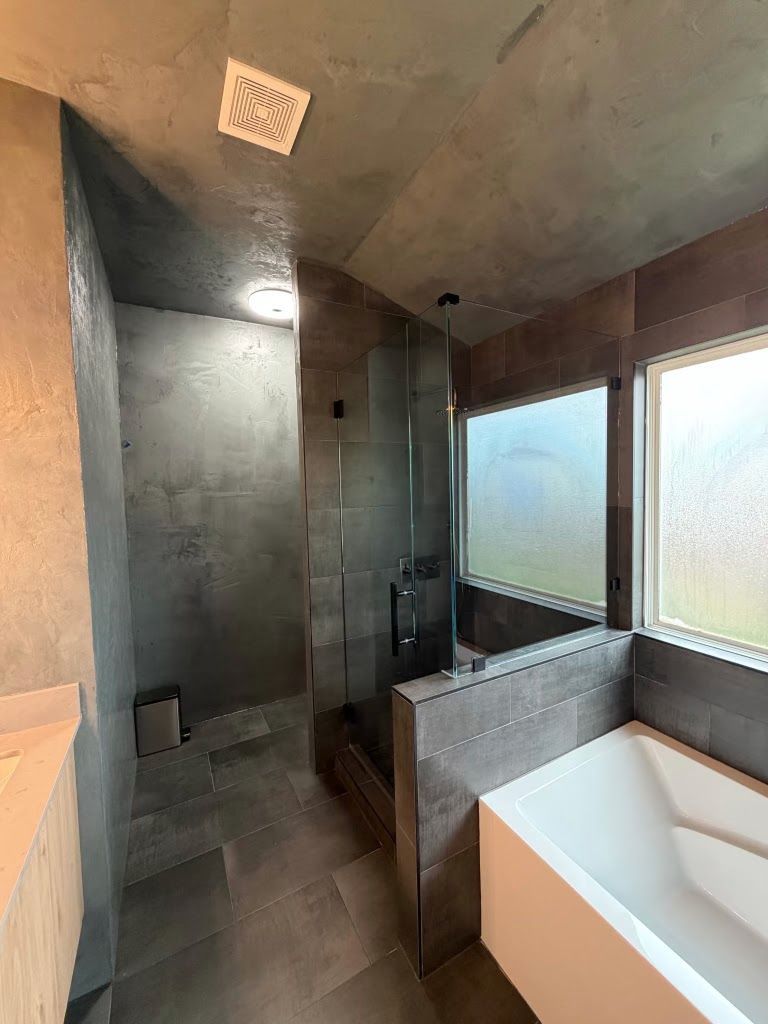 Modern bathroom with concrete walls, frosted windows, and a white bathtub beside a tiled shower.