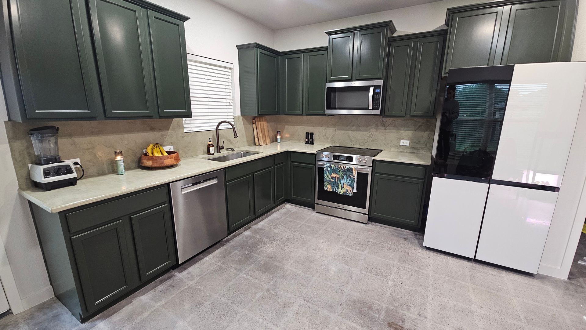 Modern kitchen with dark green cabinets, white appliances, beige counters, and light gray flooring.