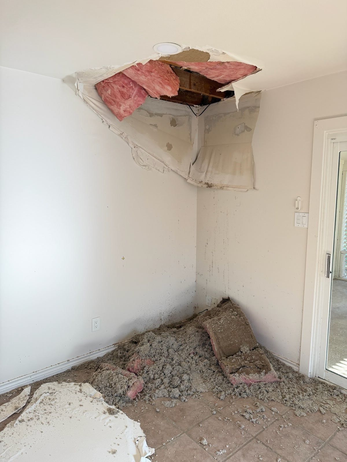 Room with a collapsed ceiling, exposed insulation, and debris piled on the floor.