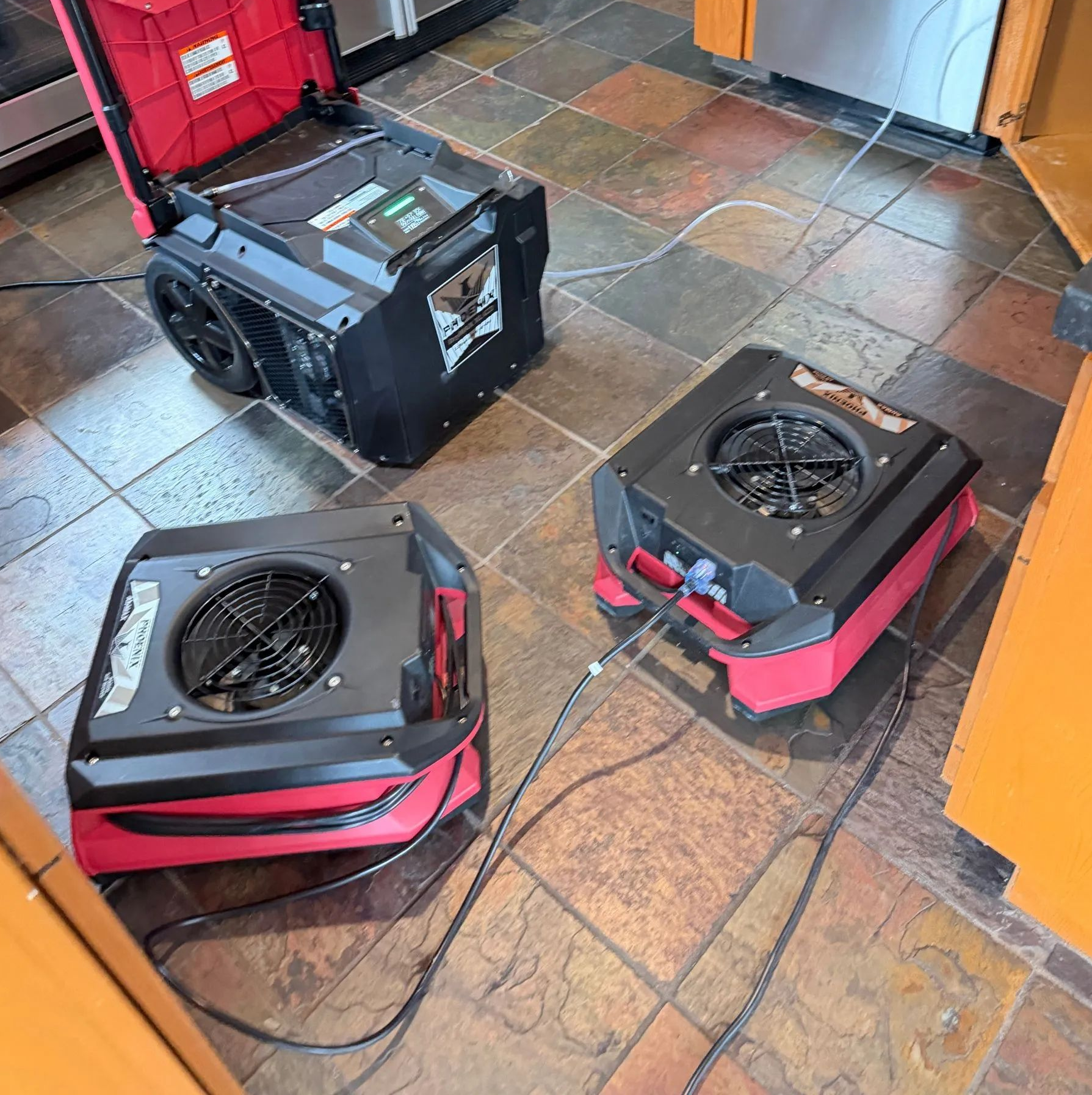 Three black-and-red box fans or heaters on a tiled floor, with cords and a red toolbox in the background
