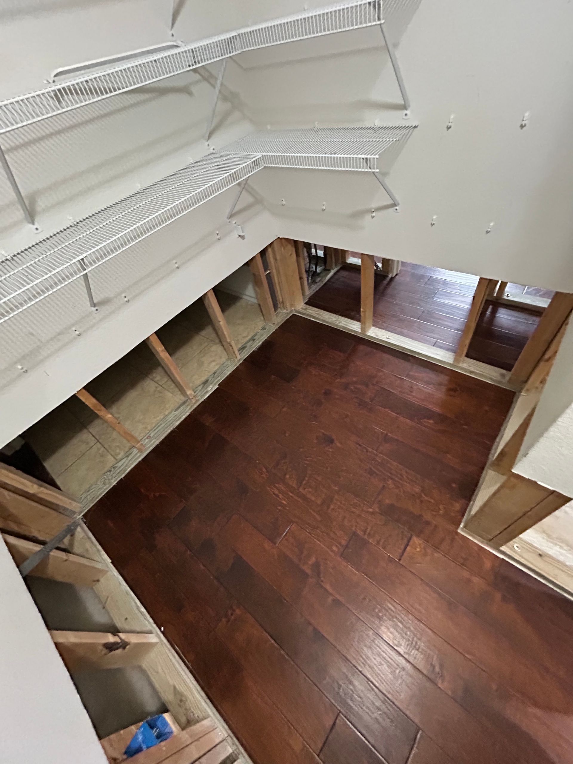 Empty walk-in closet with white wire shelves and dark wood floor, viewed from above.