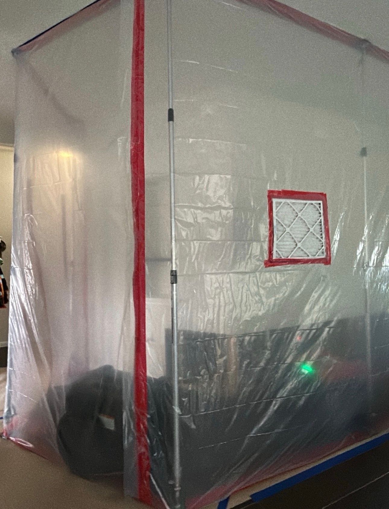 Plastic enclosed shelter with red trim and a small square window, viewed from the side inside a room