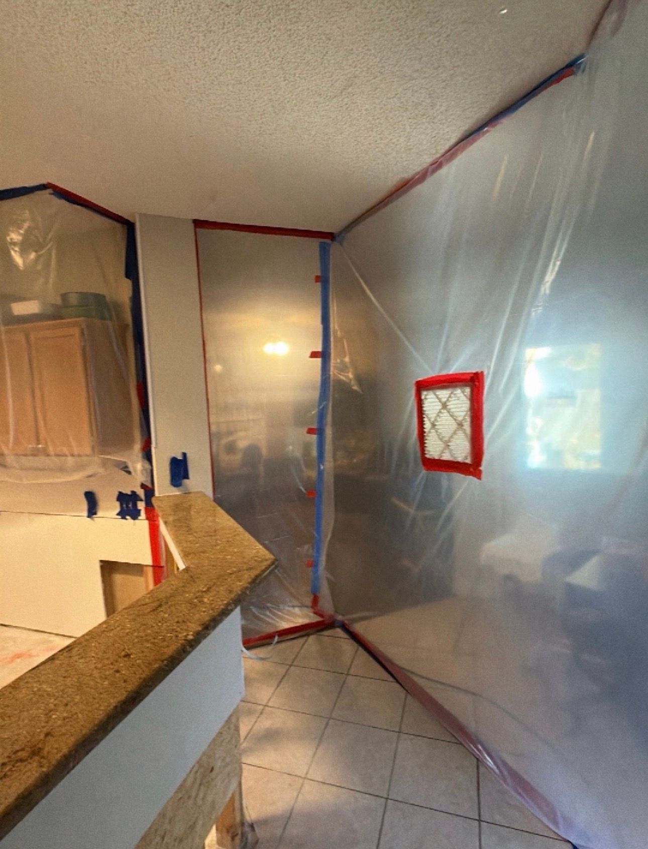 Plastic-covered interior hallway with red-taped window and tiled floor during renovation