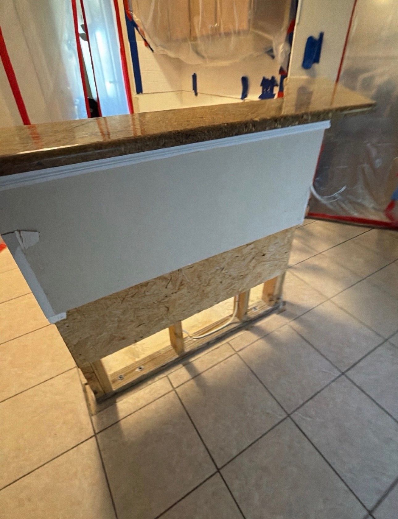 Wooden reception desk with a white front panel in a tiled lobby, reflected in a mirror behind it.