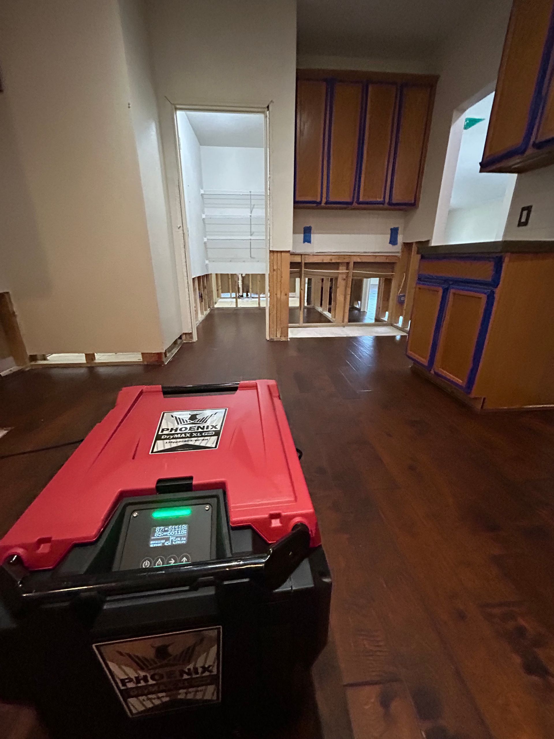 Red tool case on hardwood floor in an empty room with kitchen cabinets and a doorway beyond.