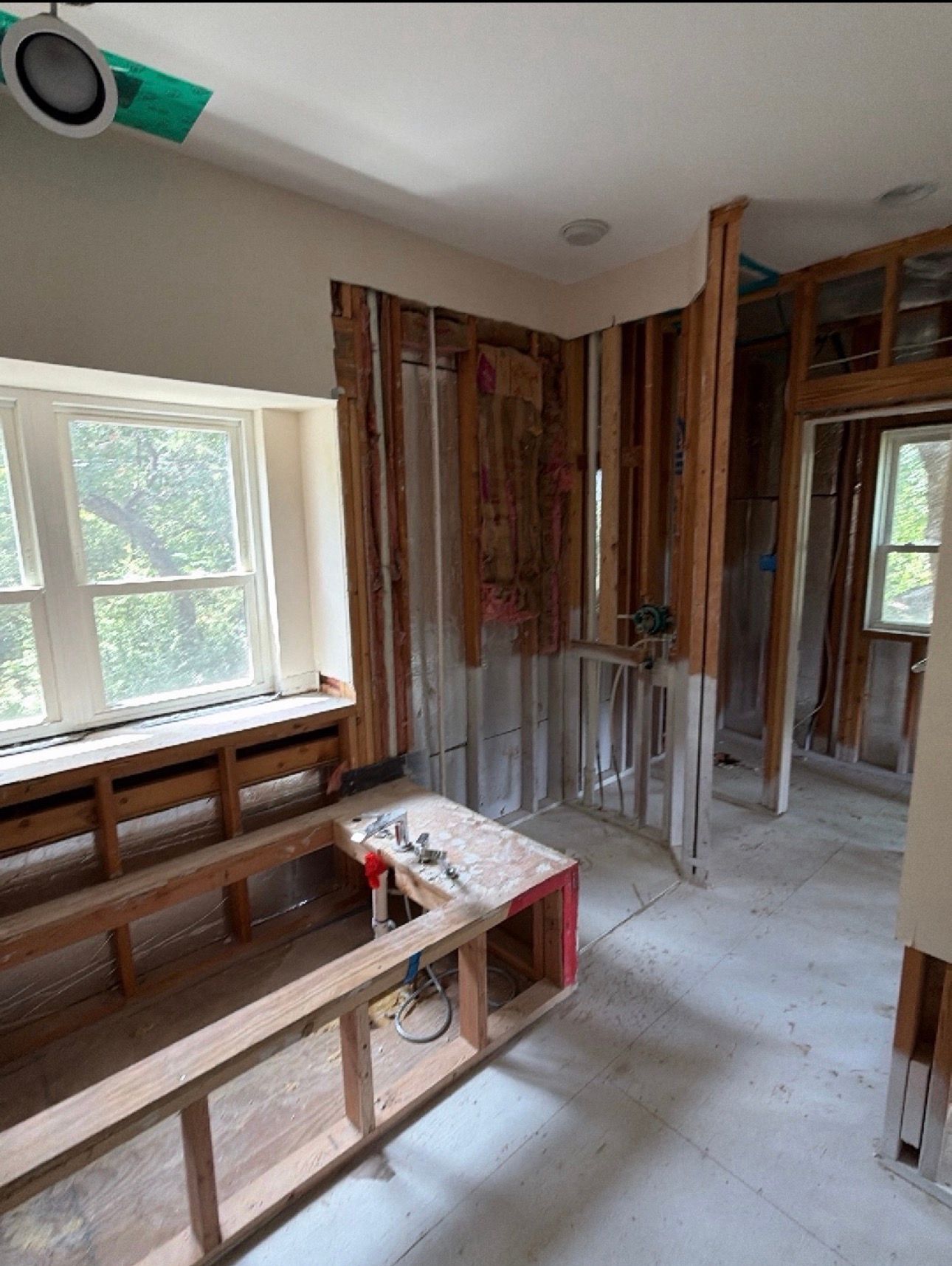 Renovation-in-progress room with exposed studs, window bench framing, and construction tools on the floor