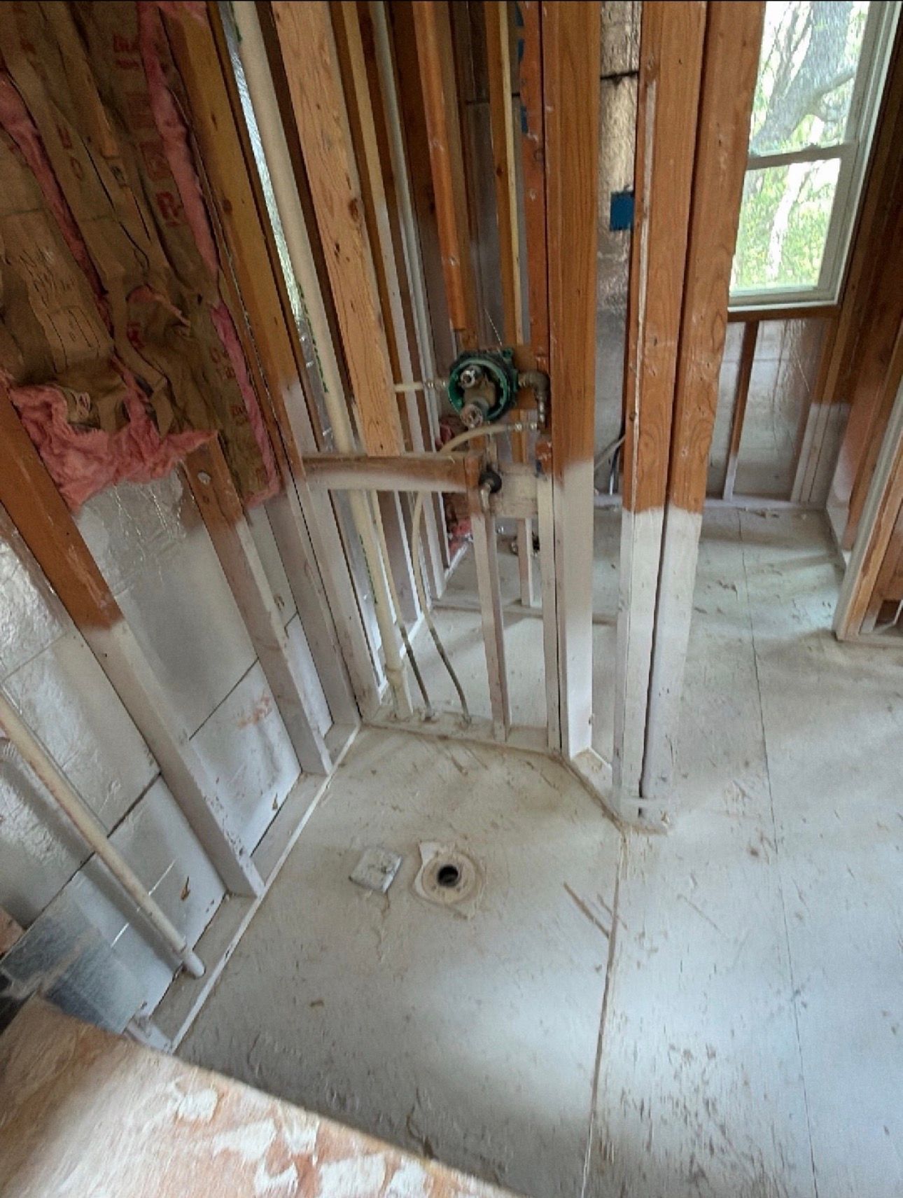 Unfinished bathroom under construction with exposed studs, plumbing, and a shower base.