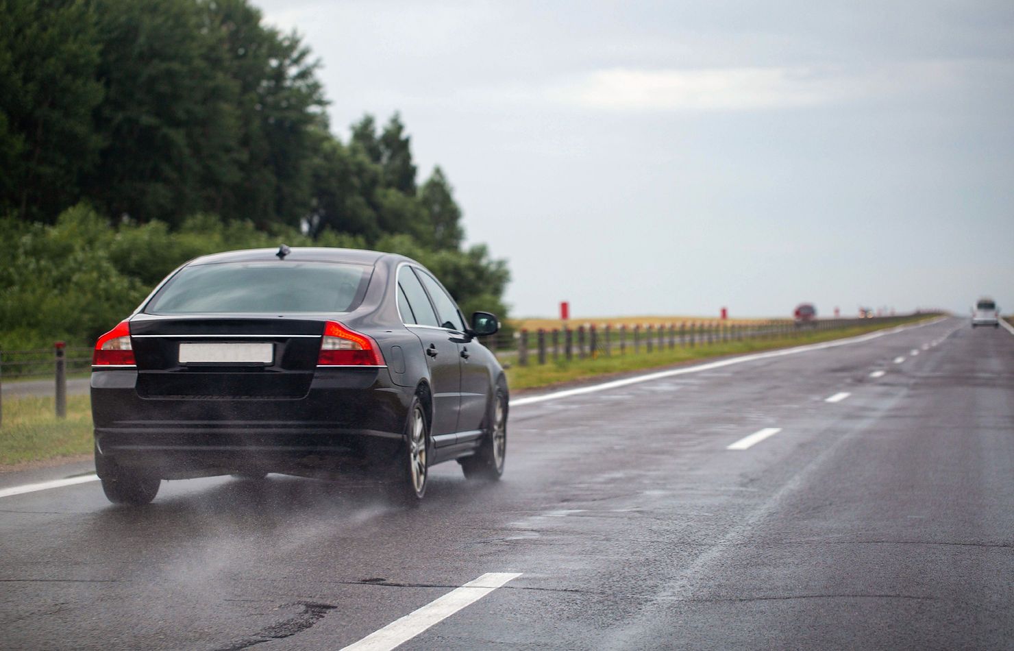 A black car is driving down a wet highway.