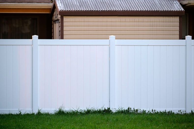 White privacy fence in front of a beige house with a green lawn at the bottom