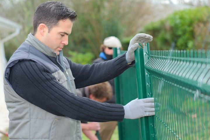 Man in gray jacket adjusting a green wire fence outdoors