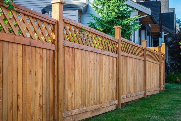 Wooden privacy fence with lattice top along a grassy backyard beside brick houses