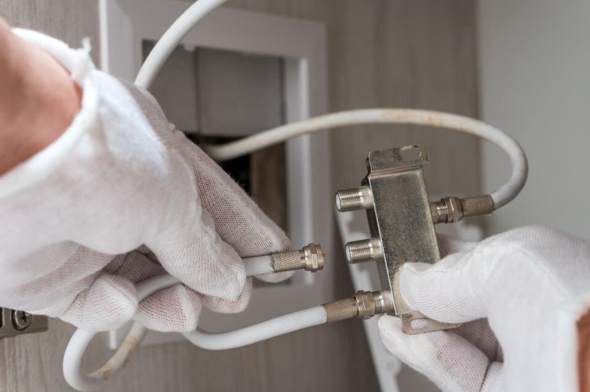 Hands In White Gloves Connecting Coaxial Cable To A Splitter In A Wall — Fry Electrical In Bateau Bay, NSW