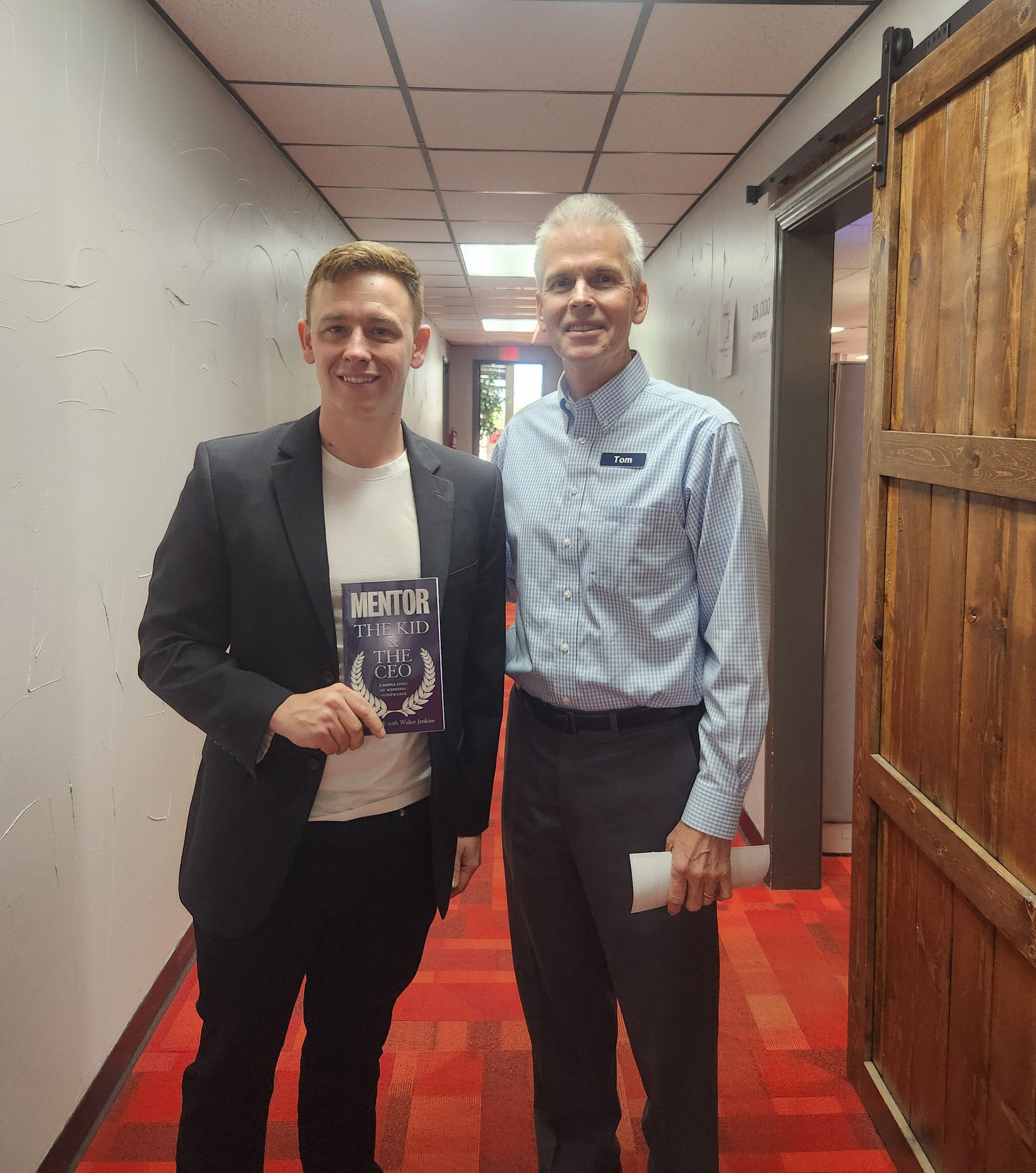 Two men standing in a hallway with one holding a book that says mental