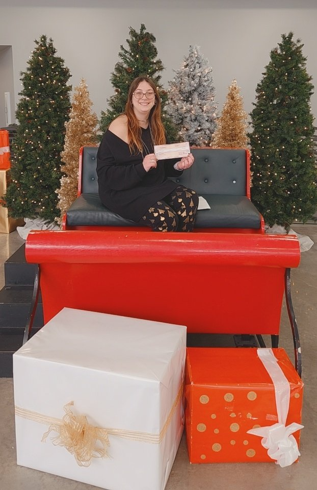 A woman is sitting on a red couch with christmas trees in the background.