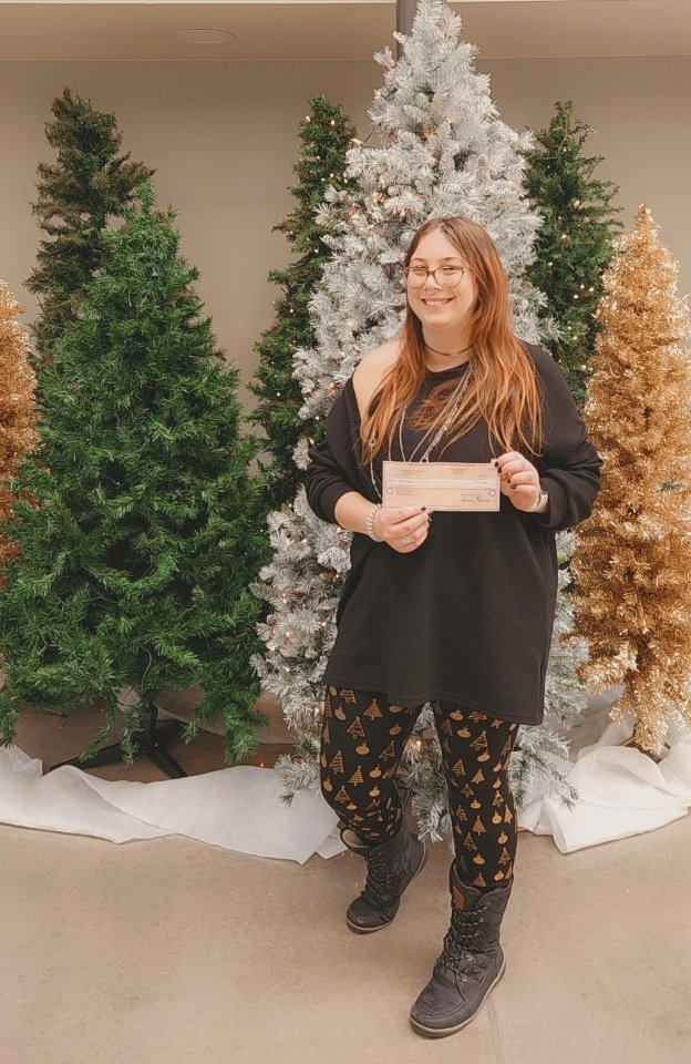 A woman is standing in front of a christmas tree holding a check.