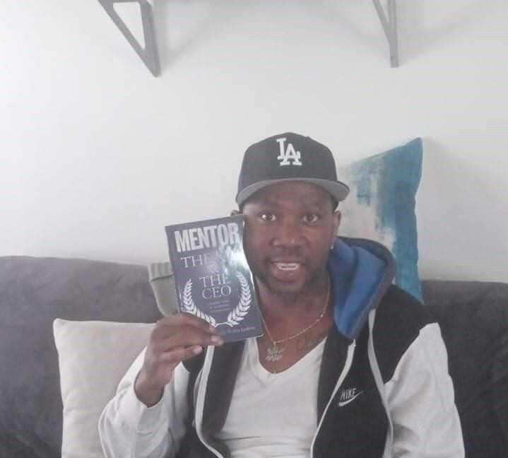 A man wearing a la hat is holding a mentor book