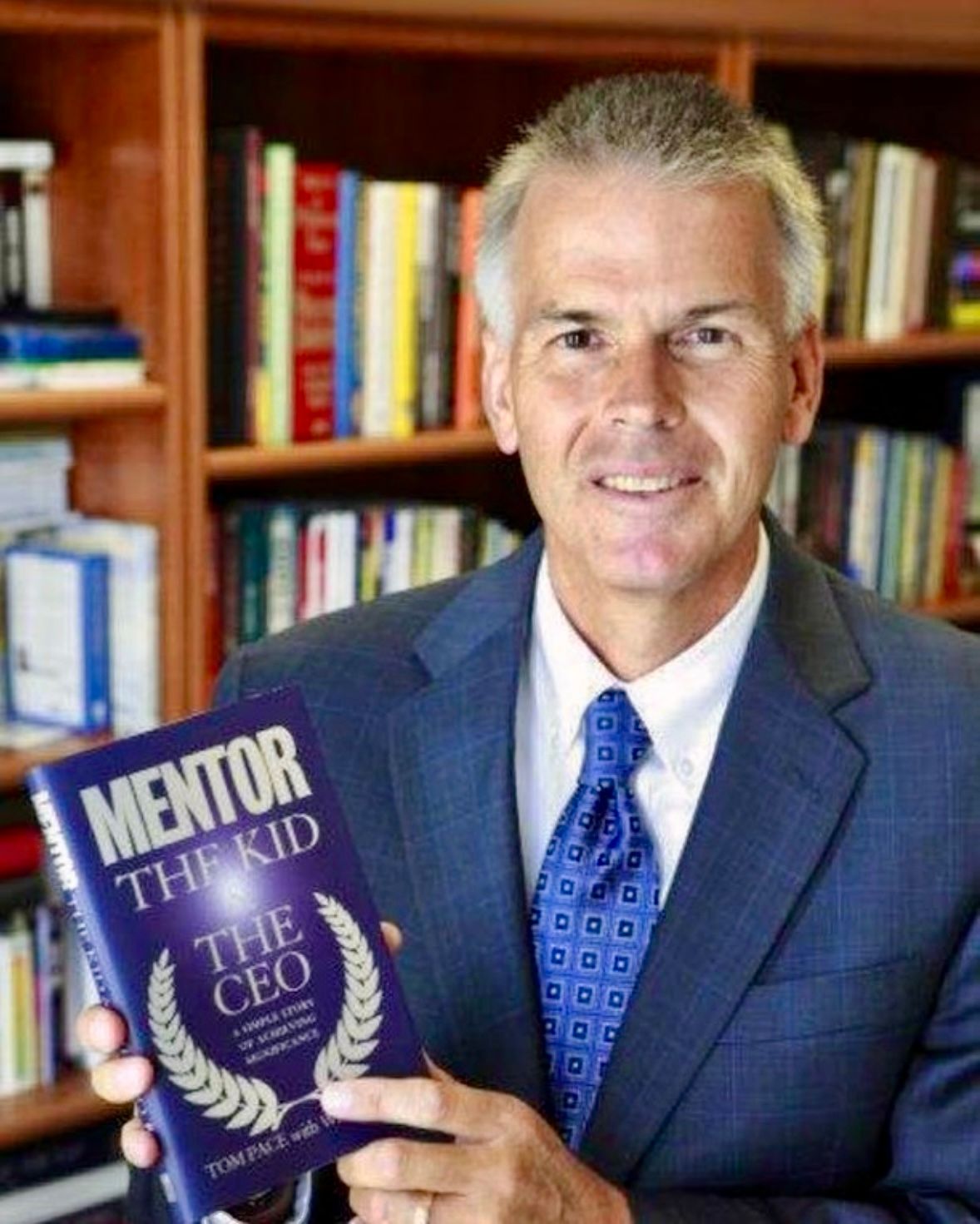 A man in a suit and tie is holding a book titled mentor the kid