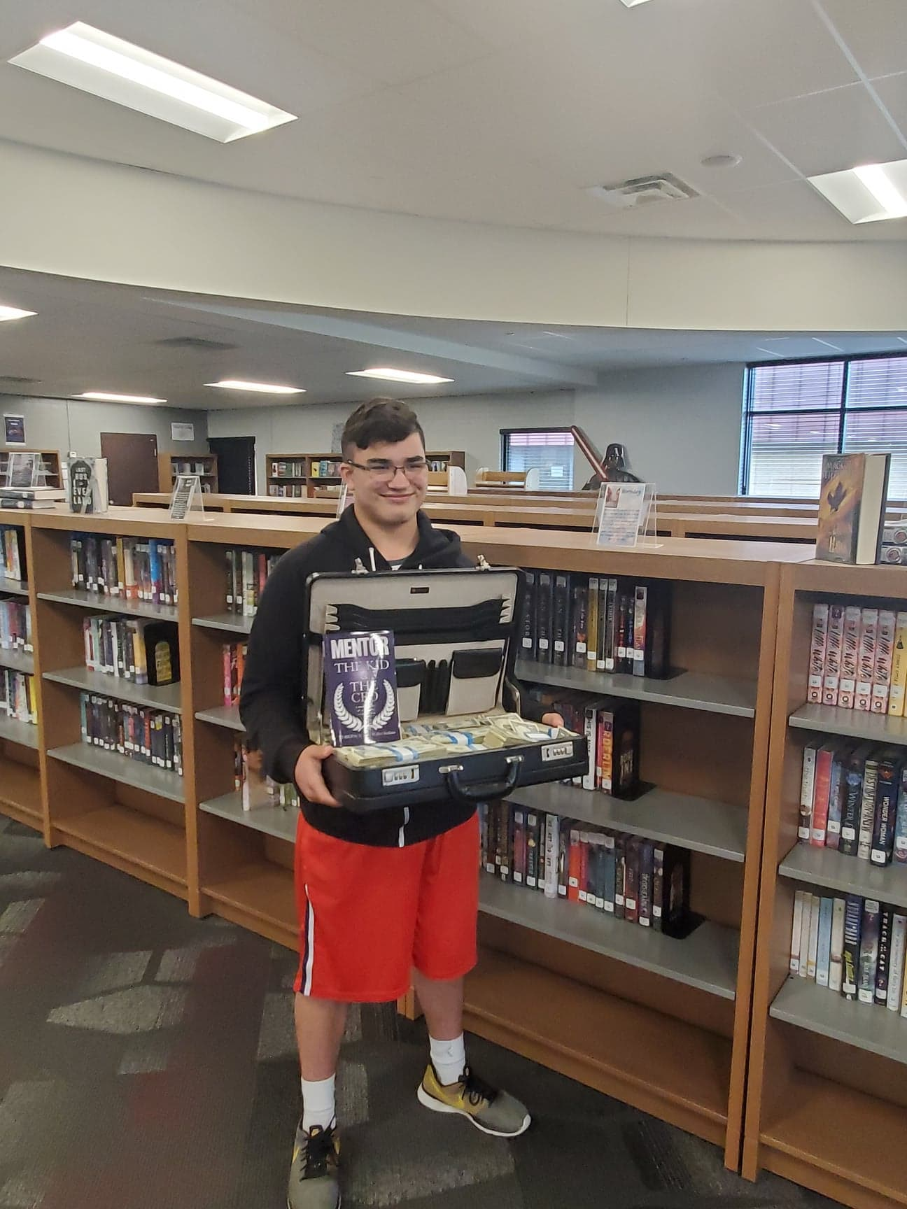 A man is holding a briefcase full of books in a library.