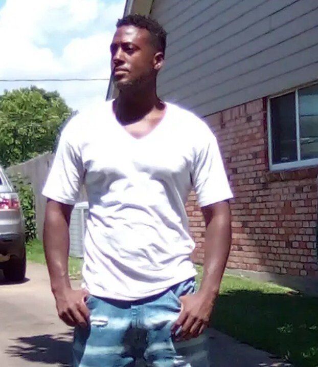 A man in a white shirt and blue jeans is standing in front of a brick house