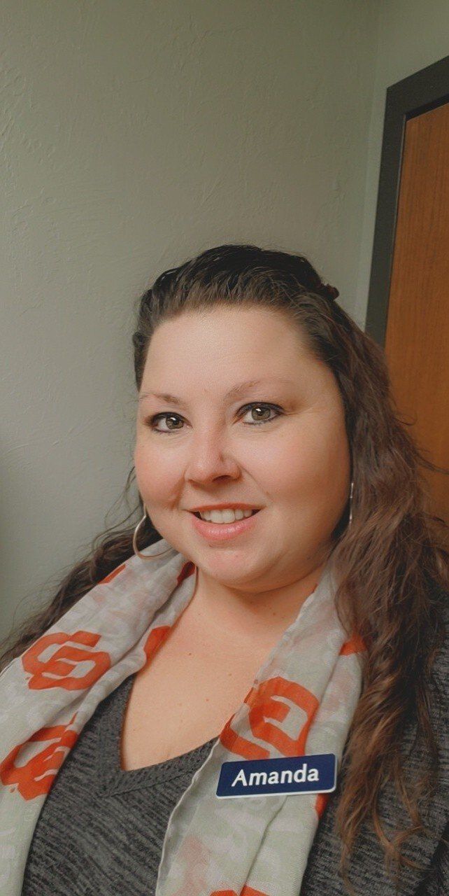A woman wearing a scarf and a name tag is smiling for the camera.