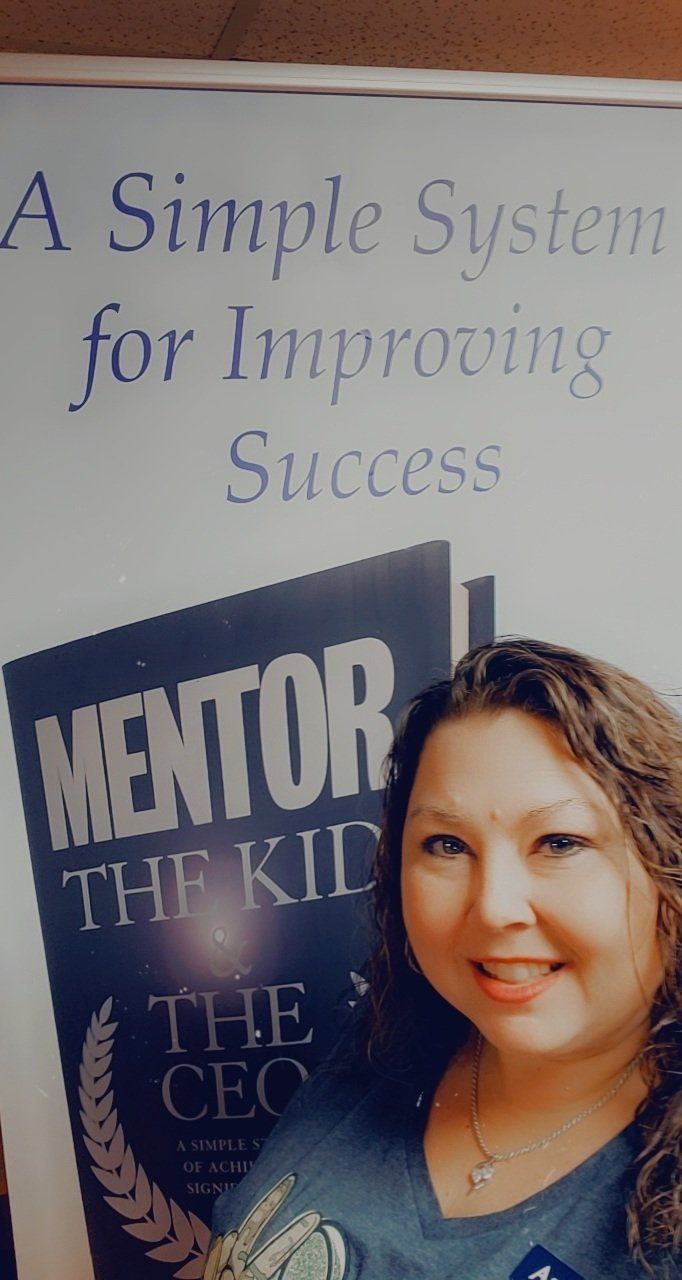 A woman is standing in front of a sign that says mentor the kid.
