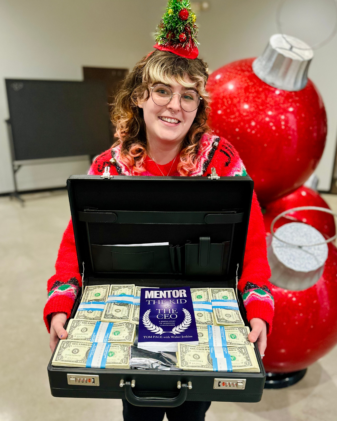 A woman in a red sweater is holding a briefcase filled with money.