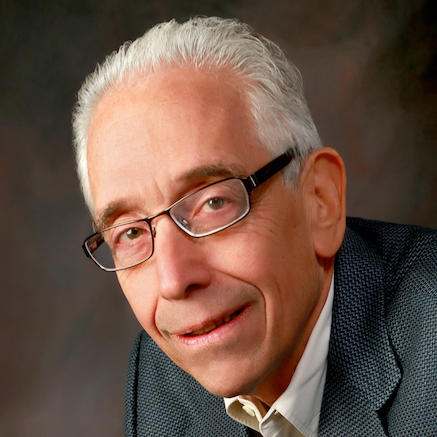 Portrait of a smiling man with glasses in a gray jacket, leaning toward the camera