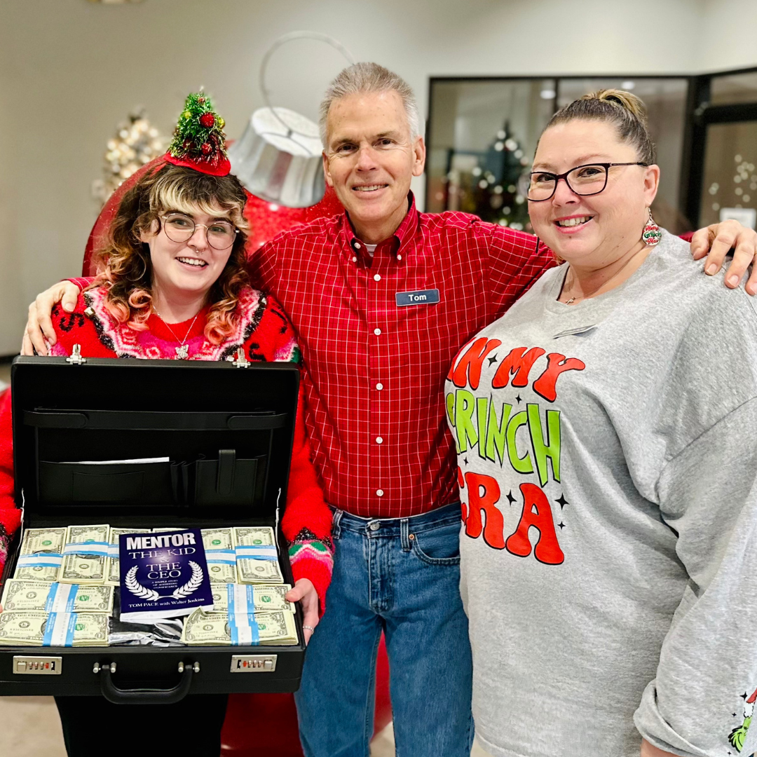 A man and two women are standing next to a briefcase filled with money.