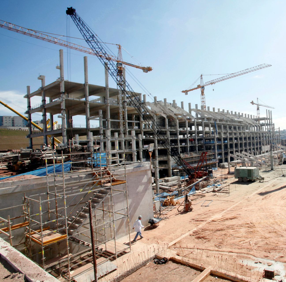 Cantiere edile con struttura in cemento armato a più piani e diverse gru sotto un cielo sereno.