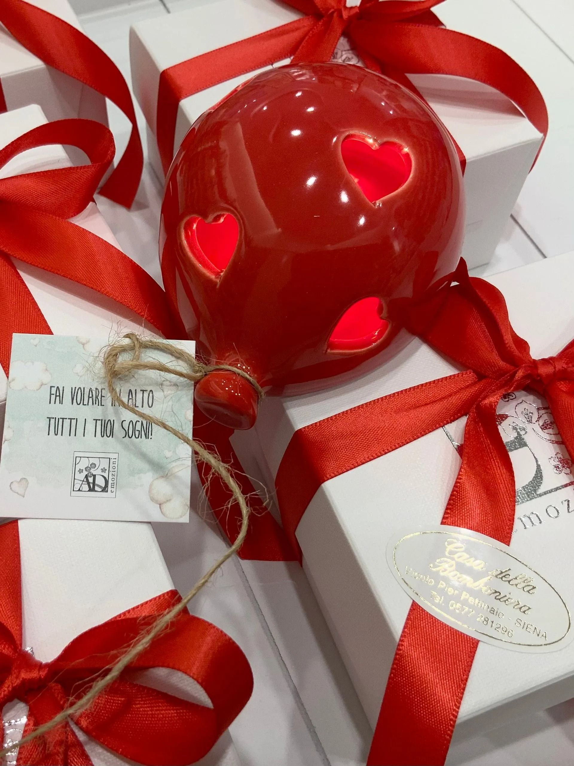 Ornamenti a forma di cuore rosso con nastro su scatole regalo bianche, decorate con piccoli cuoricini intagliati.
