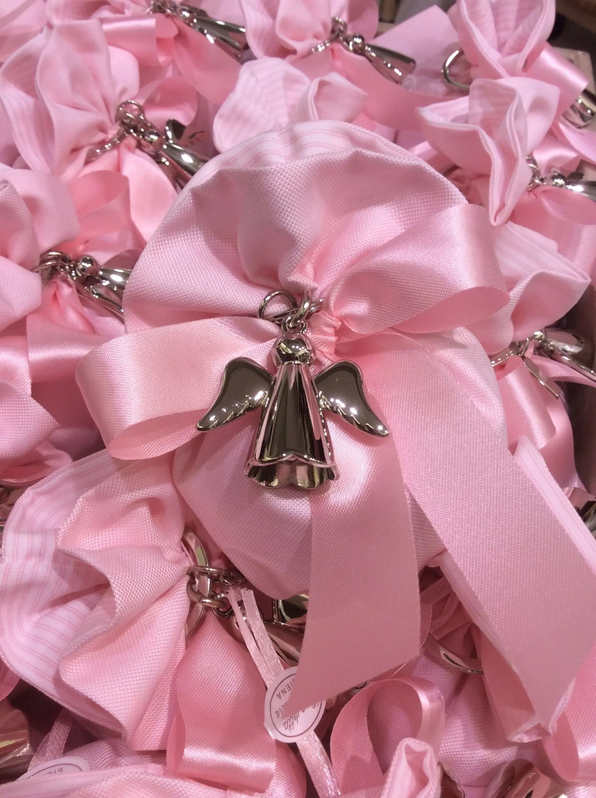 Nastri di raso rosa con piccoli ciondoli a forma di angelo argentati disposti a grappolo