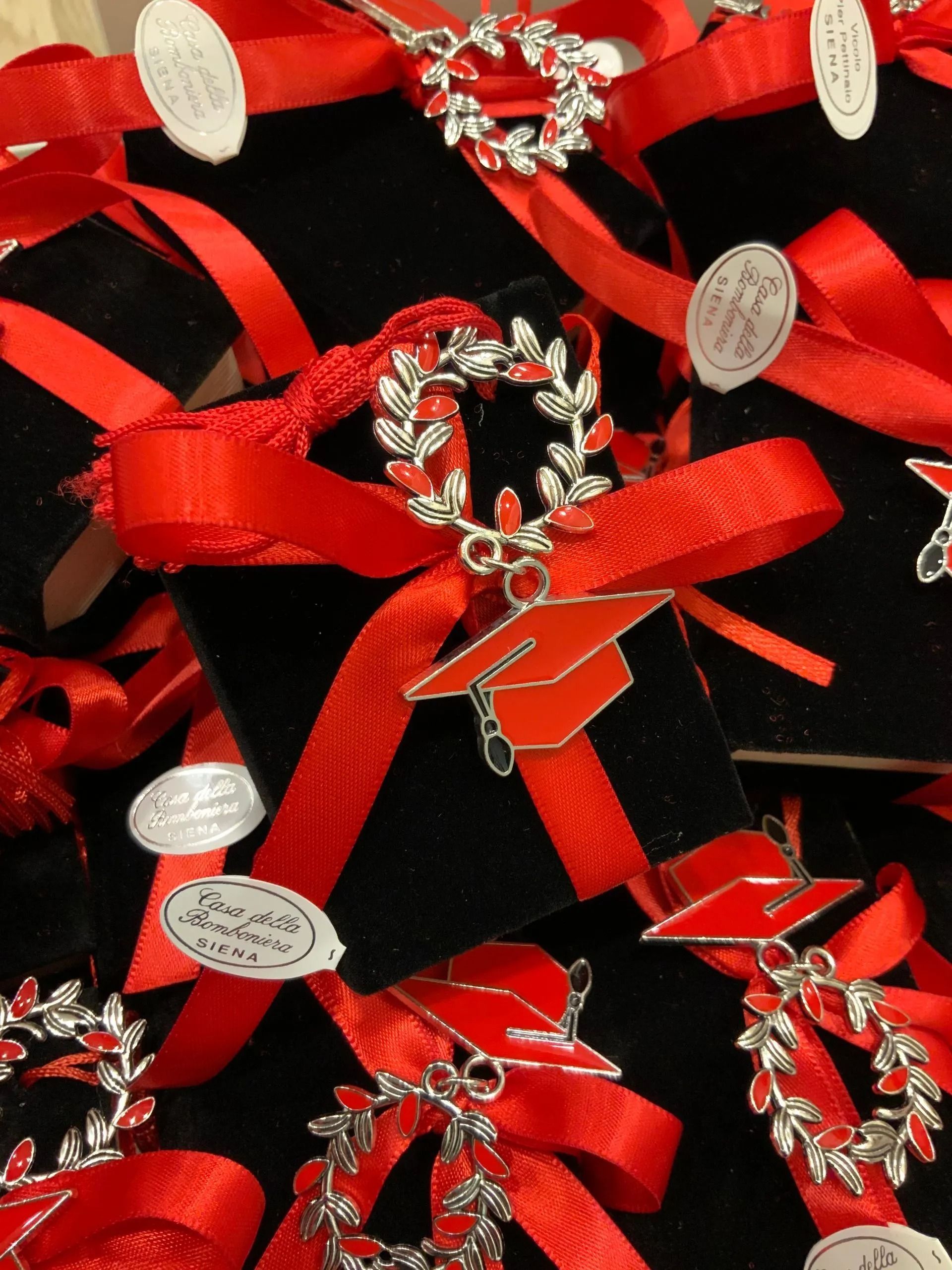 Rosette di nastro rosso con decorazioni floreali argentate disposte su tessuto nero.