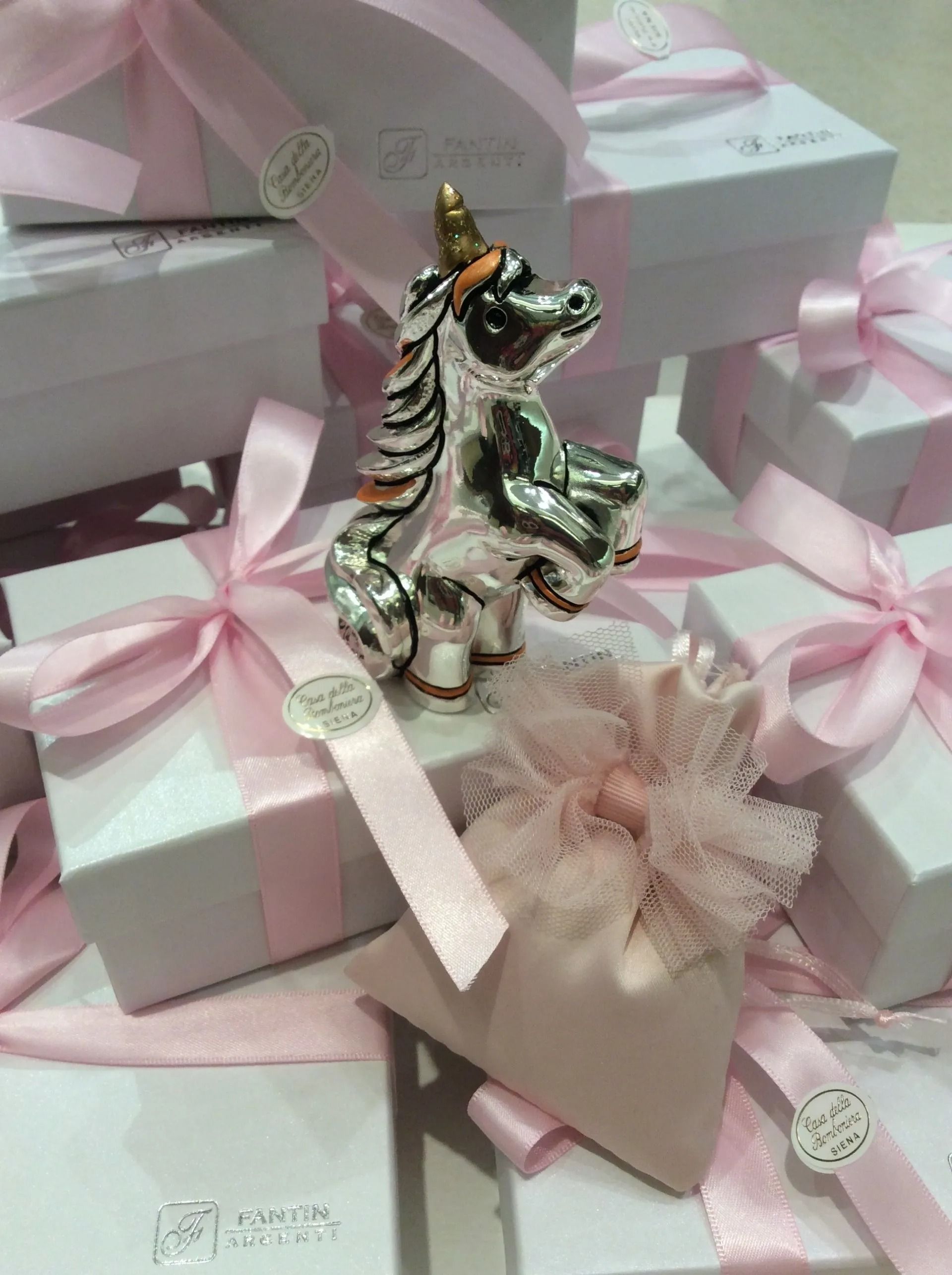 Scatole regalo impilate color pastello con nastri rosa e una piccola statuetta di unicorno argentata in cima