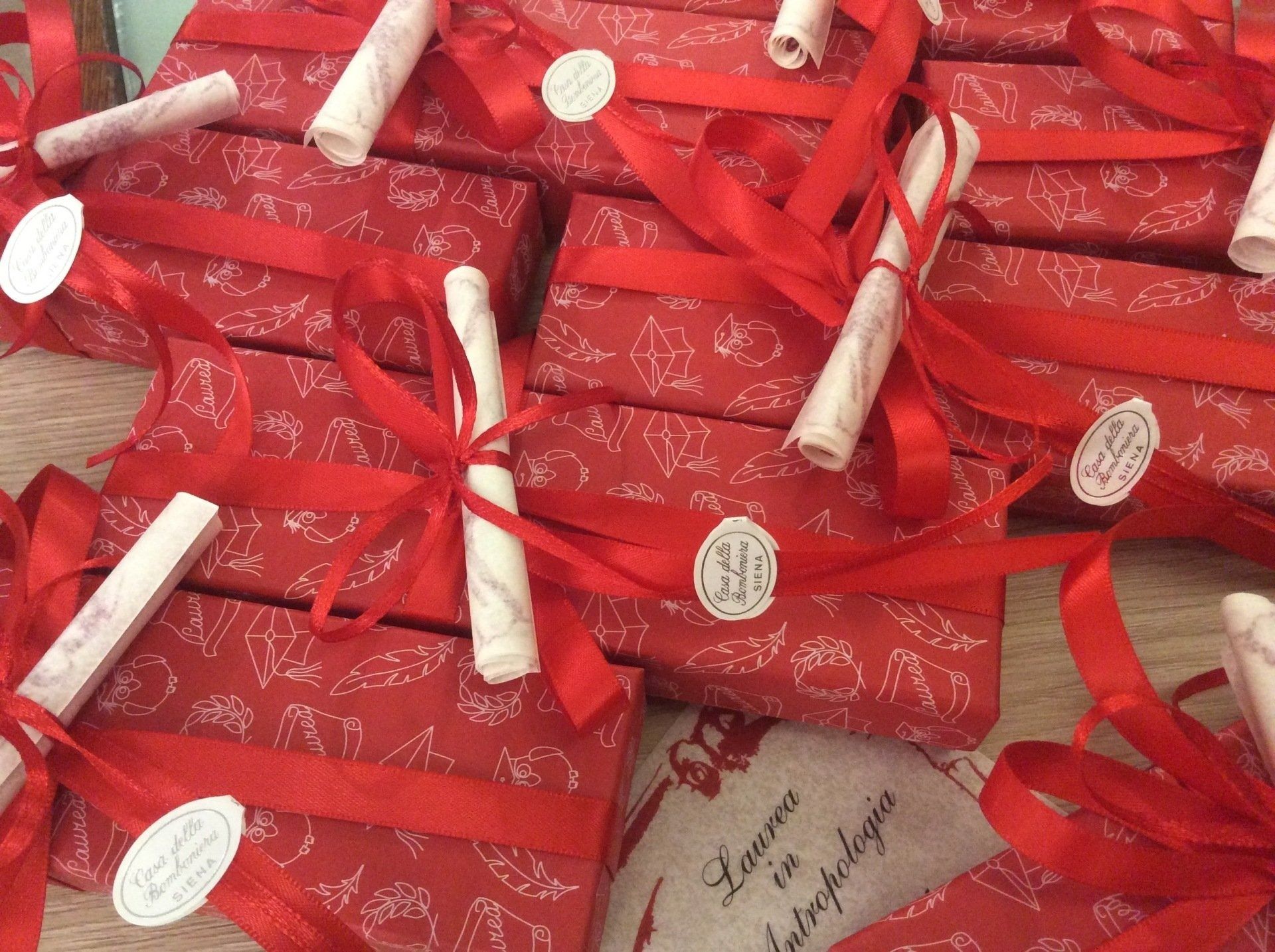 Scatole regalo rosse con nastri bianchi ed etichette ovali, impilate in una composizione festiva.