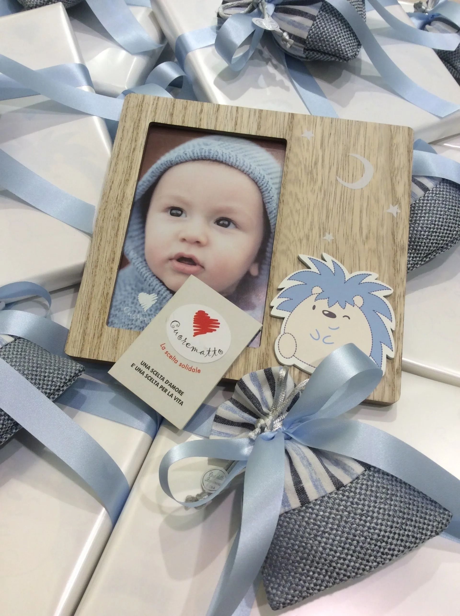 Foto di neonato in una cornice rustica con un fiocco di nastro blu e cartoncino decorativo su sfondo a righe.