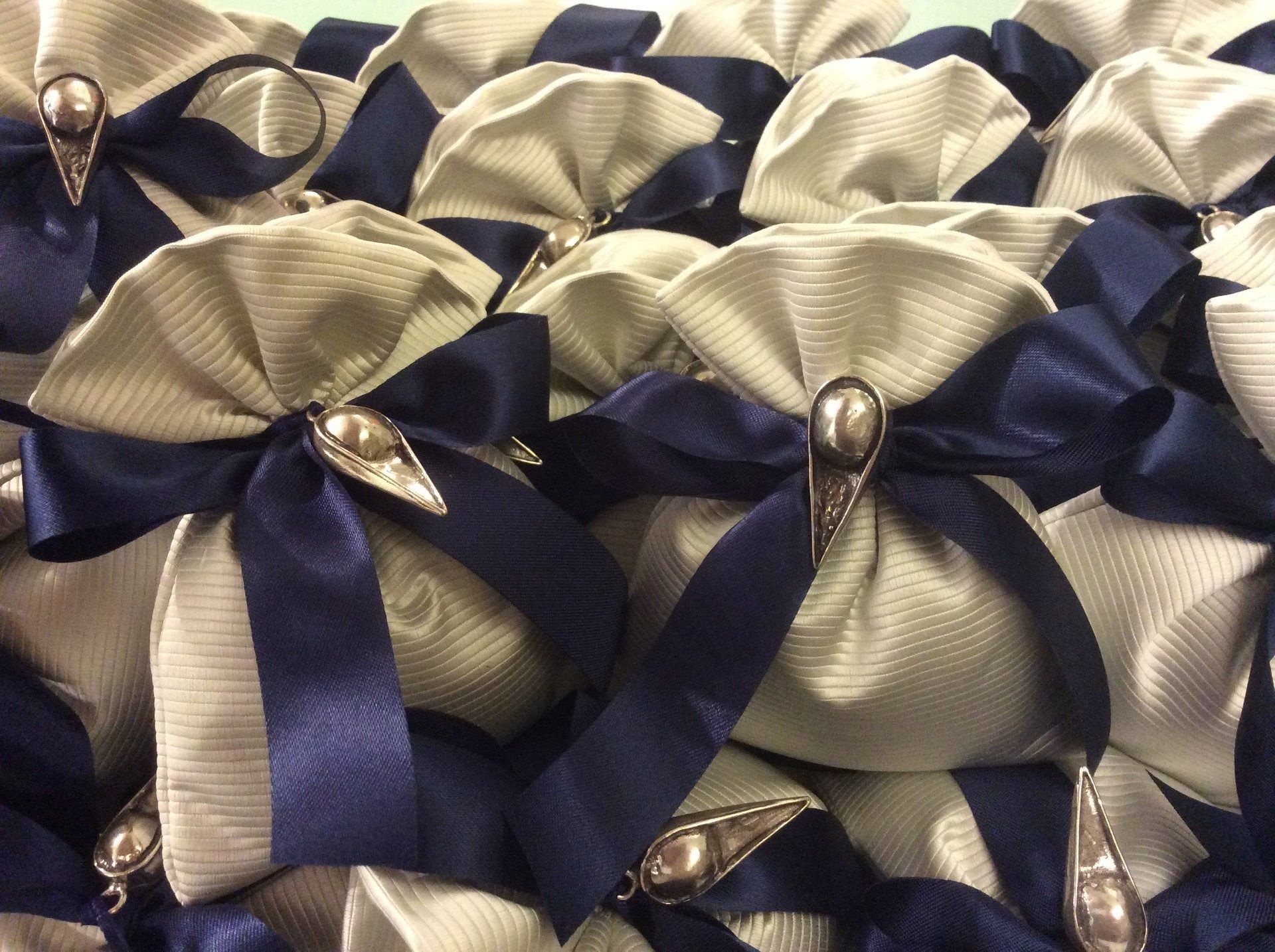 Fiocchi di nastro blu navy e avorio con centro di perle, disposti secondo un fitto motivo decorativo.